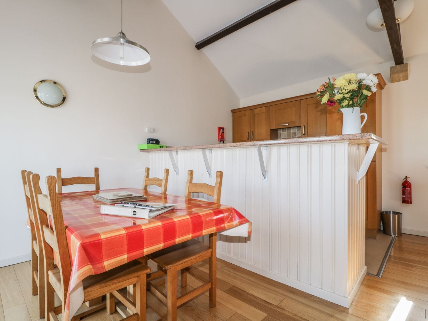 A dining area with a red and white checkered tablecloth, wooden chairs, and a pendant light.