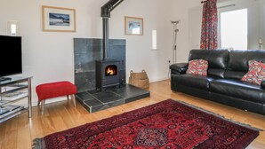 Una sala de estar con chimenea de piedra, un sofá de cuero negro, un reposapiés rojo, un televisor y una alfombra estampada.