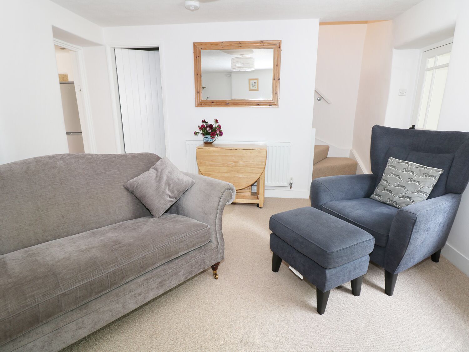 A living room with a grey sofa, a blue armchair with a patterned pillow, and a wooden side table with a vase of flowers.