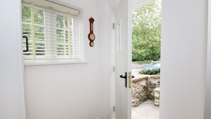 A white door leading to a garden with a stone wall and a blue car parked outside.