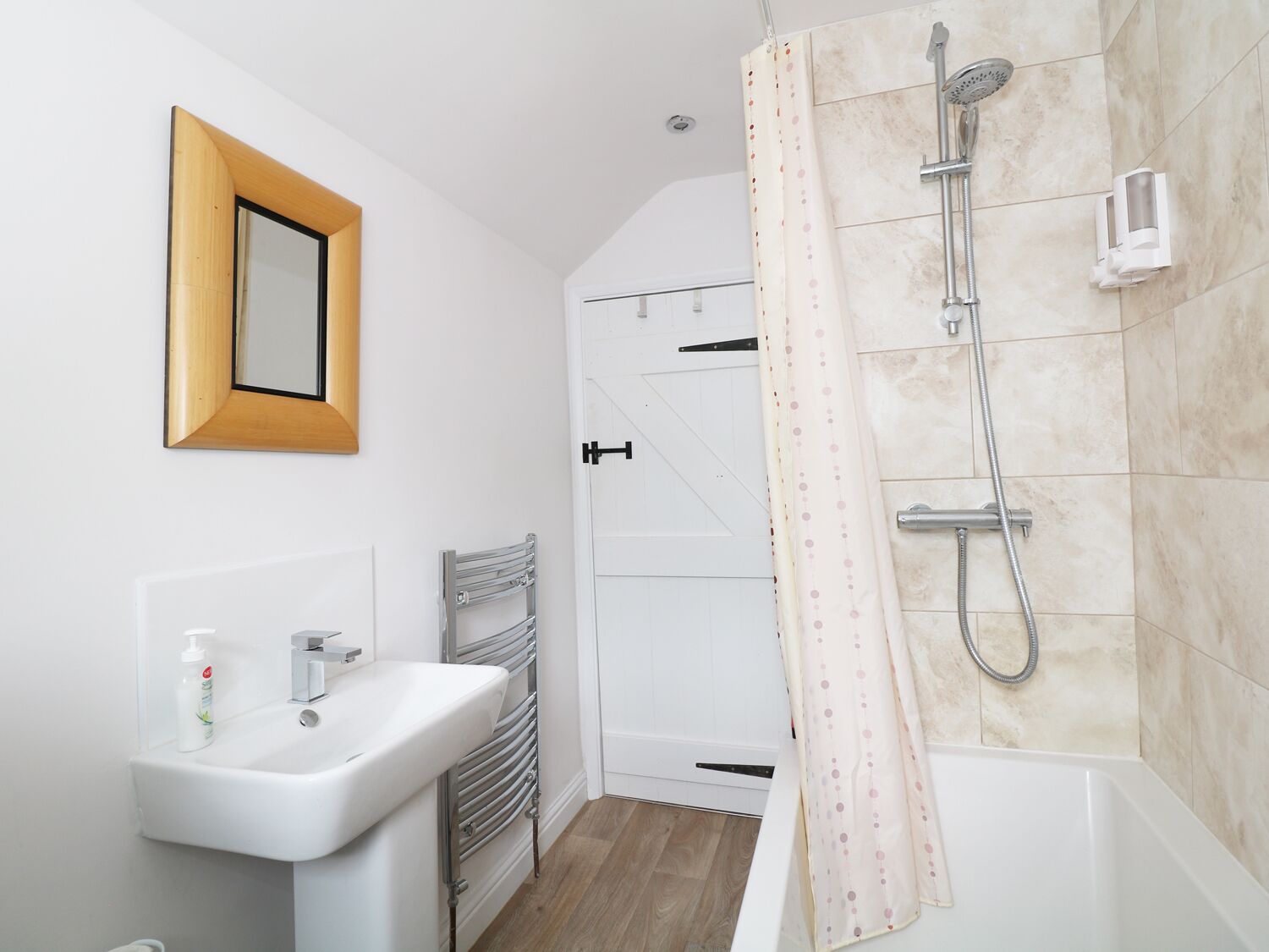 A modern bathroom with a white sink, a towel rack, a shower with a handheld showerhead, and a toilet.