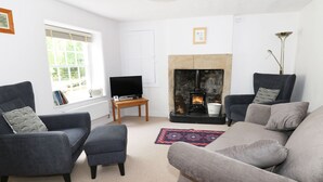 A living room with a fireplace, two armchairs, a sofa, a television, and a window with blinds.