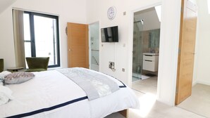 A bedroom with a bed, a TV, a wooden door, and a bathroom visible through an open door. - 7 Ocean Gateway (Hythe)