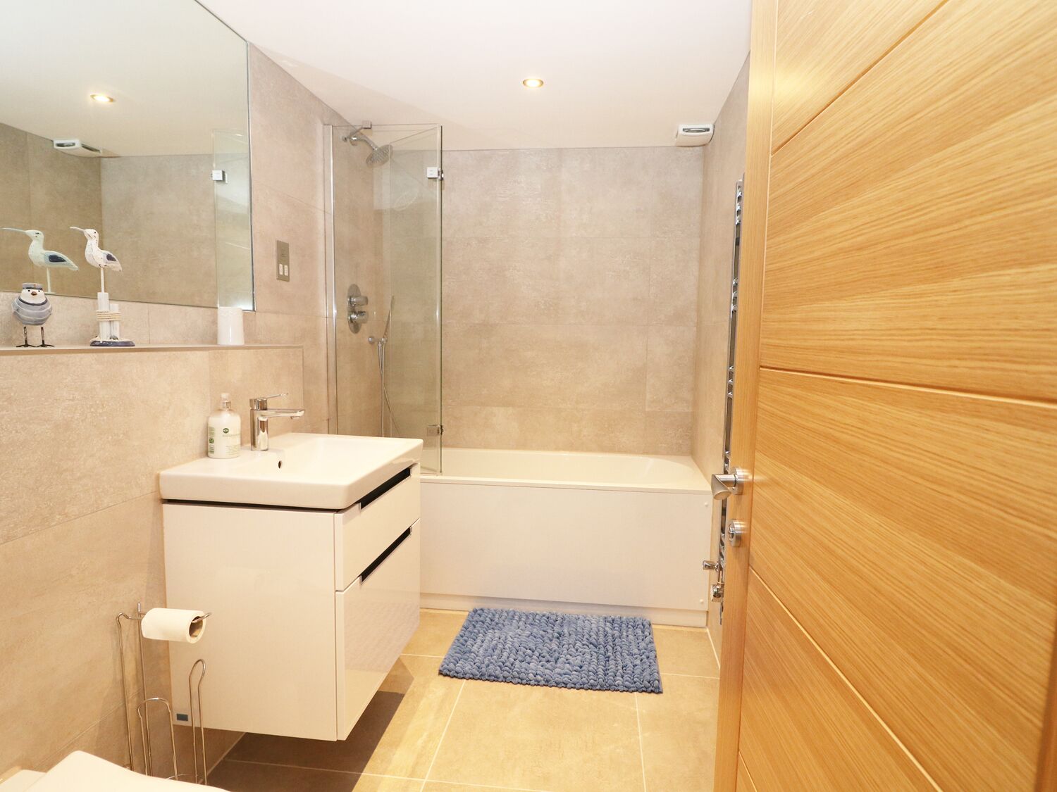Un bagno moderno con box doccia in vetro, lavandino bianco e porta in legno.
