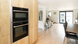 A modern kitchen with built-in ovens and a dining area with a wooden table and chairs. - 7 Ocean Gateway (Hythe)