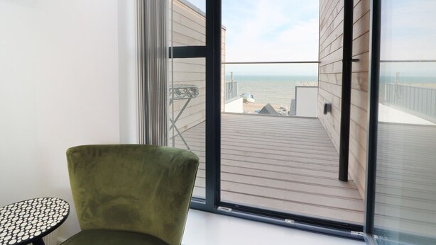 A balcony with a view of the sea, a green chair, and a small table. - 7 Ocean Gateway (Hythe)