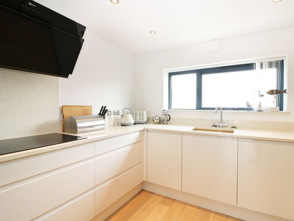 A modern kitchen with white cabinetry, a black range hood, a window with blinds, and a countertop with a kettle and toaster.
