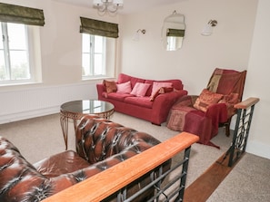 Uma sala de estar com um sofá vermelho, uma poltrona de couro, um banco de madeira e uma mesa de vidro redonda.