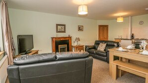 Una sala de estar con un sofá de cuero negro, una televisión, una chimenea y un comedor con una mesa dispuesta para dos.