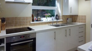 A modern kitchen with a built-in oven, a sink, and a window with a view of greenery. - Stones Throw (Truro)