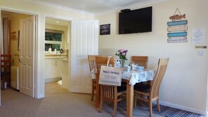 A dining area with a table set for four, a television mounted on the wall, and a sign with holiday advice. - Stones Throw (Truro)