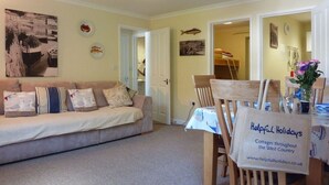 A cozy living room with a sofa, a dining table with chairs, and a sign advertising cottages in the West Country. - Stones Throw (Truro)