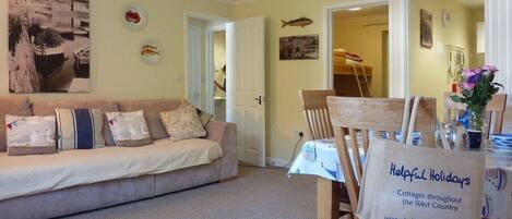 A cozy living room with a sofa, a dining table with chairs, and a sign advertising cottages in the West Country.
