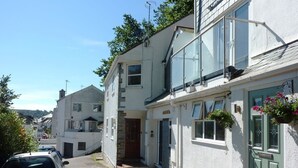 A narrow street with white houses, a parked car, and a clear sky. - Stones Throw (Truro)