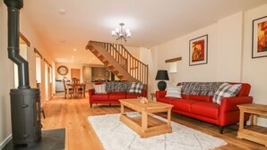 Ein großzügiges Wohnzimmer mit einem roten Sofa, einem Holztisch und einem schwarzen Herd. Eine Treppe führt in den Hintergrund zu einer Küche.