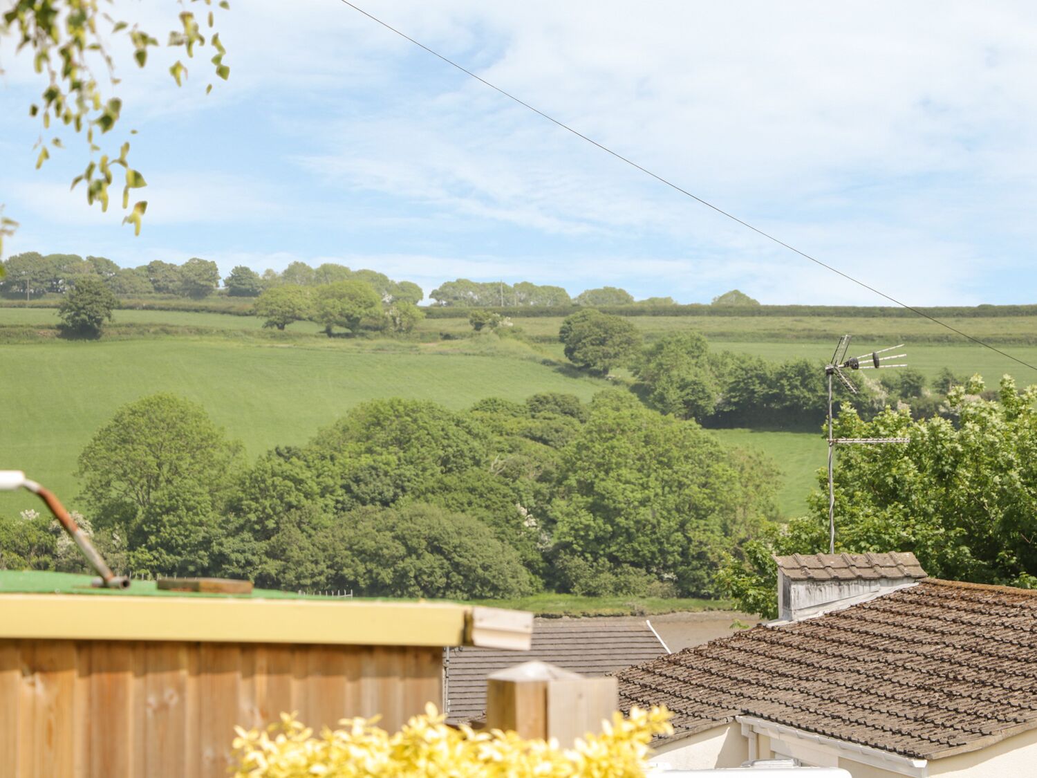A rural landscape with a clear sky, a wooden fence, and a building with a tiled roof.