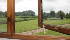 A view through a wooden-framed window of a grassy field with a distant tree line. - The Old Goat Barn at Trout Cottage (Somerton)