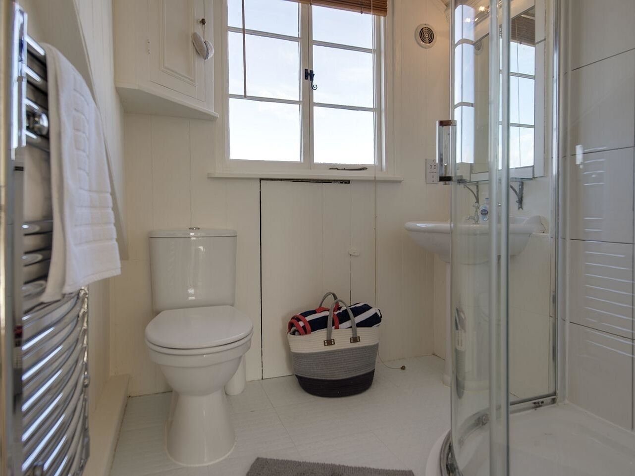 Un bany amb vàter, un espai de dutxa amb envàs de vidre, un lavabo blanc i una finestra sobre el vàter.