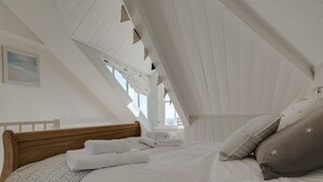 A bedroom with a sloped ceiling, a wooden bed frame, white bedding, and star-patterned pillows. - 1 Florence Place (Falmouth)