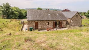 A stone farmhouse with a sloped roof, a small porch, and a fenced yard. - The Barn (Abergavenny)