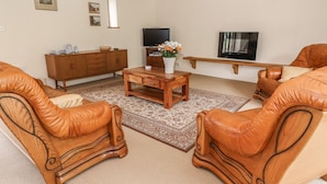 A living room with leather armchairs, a wooden coffee table, a TV, and a cabinet. - The Barn (Abergavenny)