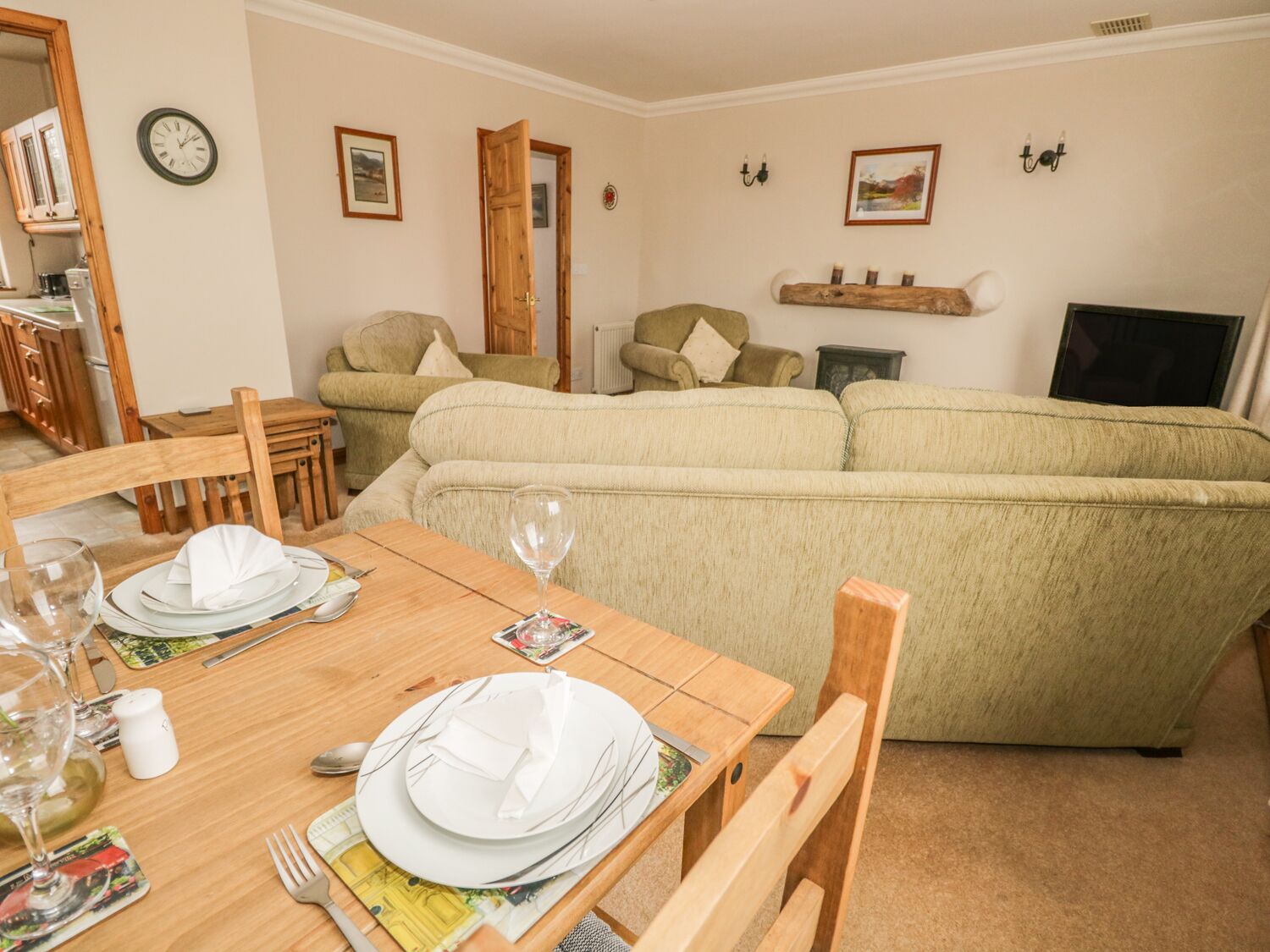 A dining area with a wooden table set for four, a sofa, and a television in the background.