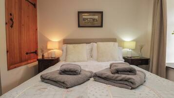Quarto de hotel com cama, duas luminárias de cabeceira, um guarda-roupa de madeira, um quadro na parede e uma janela com cortinas.