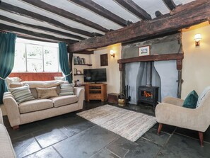 A cozy living room with a fireplace, a sofa, a television, and a stone floor. - Rose Cottage (Broughton in Furness)