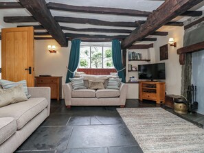 A cozy living room with a sofa, a television, and a fireplace. - Rose Cottage (Broughton in Furness)
