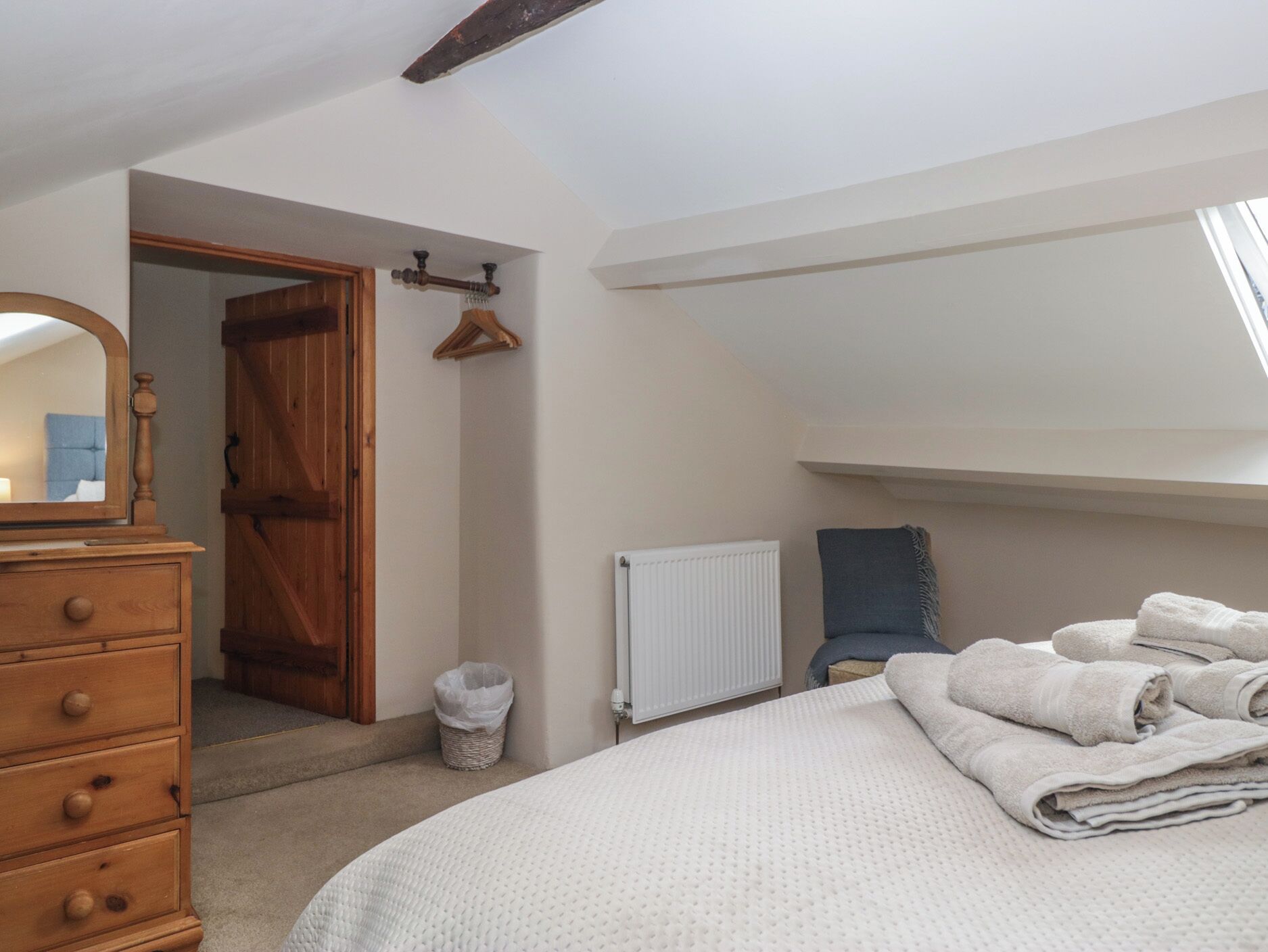 A bedroom with a wooden dresser, a bed with white bedding, a radiator, and a window.