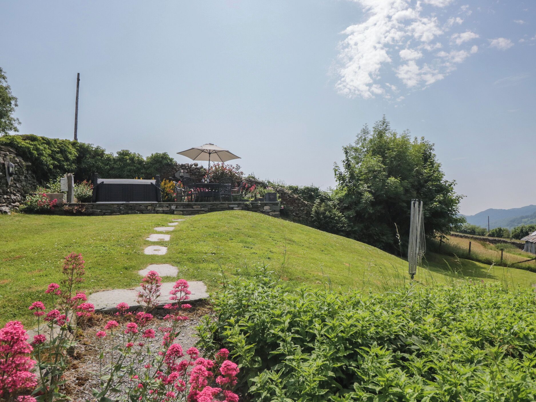 A grassy outdoor area with a stone pathway leading to a seating area with an umbrella.