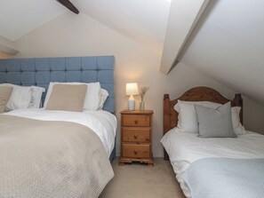A bedroom with two beds, a nightstand with a lamp, and a wooden headboard. - Rose Cottage (Broughton in Furness)