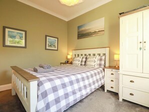 A bedroom with a checkered bedspread, two bedside tables with lamps, a wardrobe, and two framed pictures on the wall. - Seashore House (Newquay)