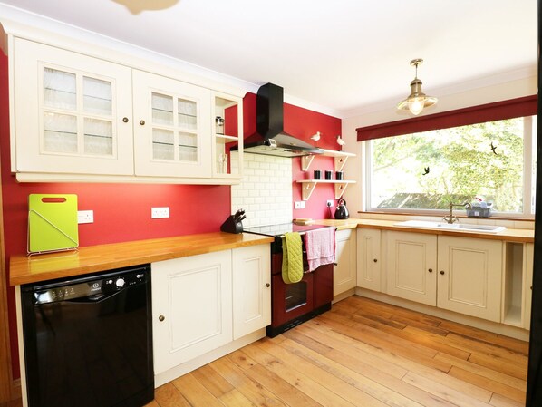 A kitchen with white cabinets, a red wall, a wooden countertop, a dishwasher, and a window with a view of greenery.
