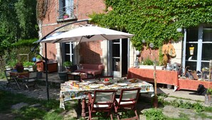 Un área de comedor al aire libre con una mesa dispuesta para una comida, rodeada de sillas y una sombrilla.
