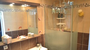 Un baño con ducha envuelta en vidrio, un lavamanos con espejo y artículos de aseo en la encimera.