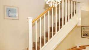 A staircase with white railings and wooden handrails, carpeted steps, and a chandelier.