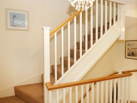 A staircase with white railings and wooden handrails, carpeted steps, and a chandelier.