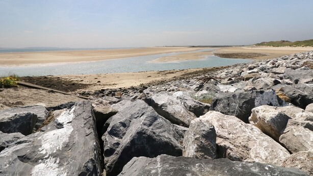 A rocky beach with a clear view of the sea and distant hills.