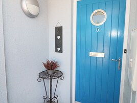 A blue door with the number 5, a small potted plant on a metal table, and a wall-mounted light fixture.