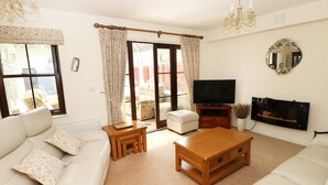 A living room with a sofa, coffee table, TV, fireplace, and large windows with curtains.