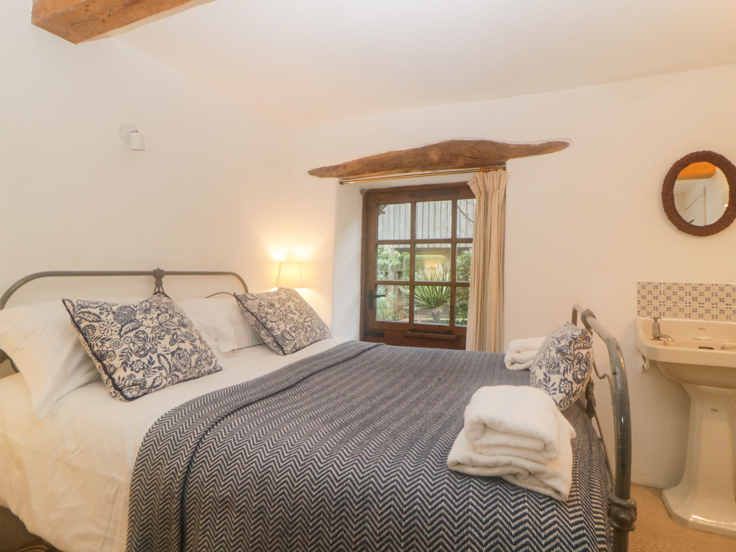 Une chambre à coucher comprenant un lit, des oreillers, une table de chevet, une fenêtre et une salle de bain avec un lavabo et un miroir.