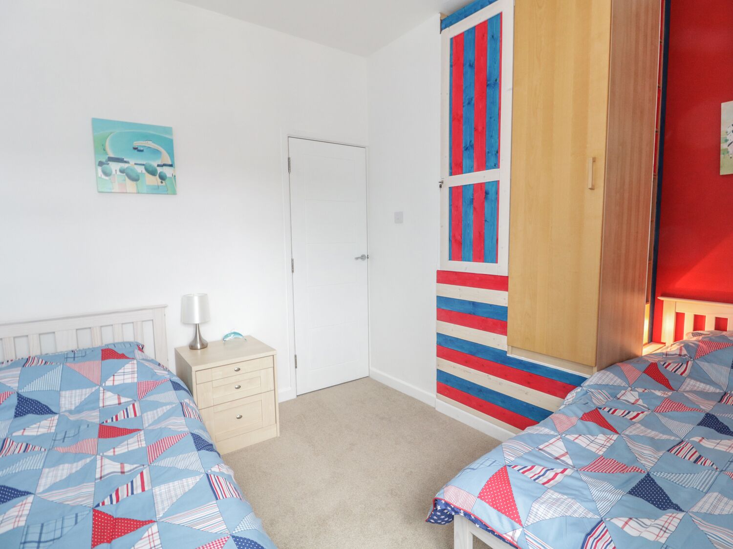 Een slaapkamer met twee bedden, een nachtkastje, een deur en een muur met strepen.