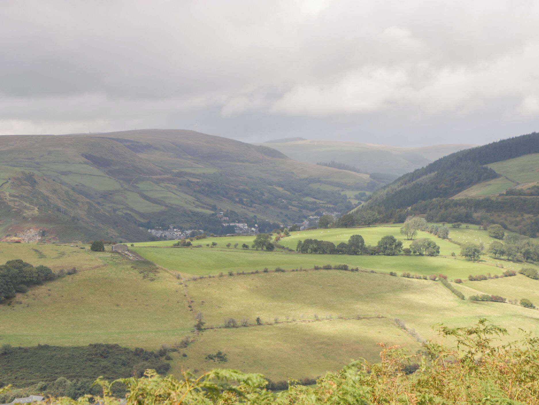 A rural landscape with rolling hills, a small village, and a clear sky.