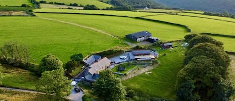 An aerial view of a rural property with multiple buildings, including a main house and several outbuildings, surrounded by expansive green fields and rolling hills.