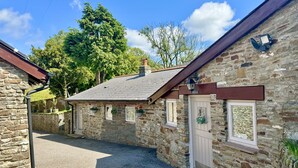 A stone building with a gravel driveway, a door, and a window with a hanging flower basket. - Caner Bach Lodge (Bridgend)