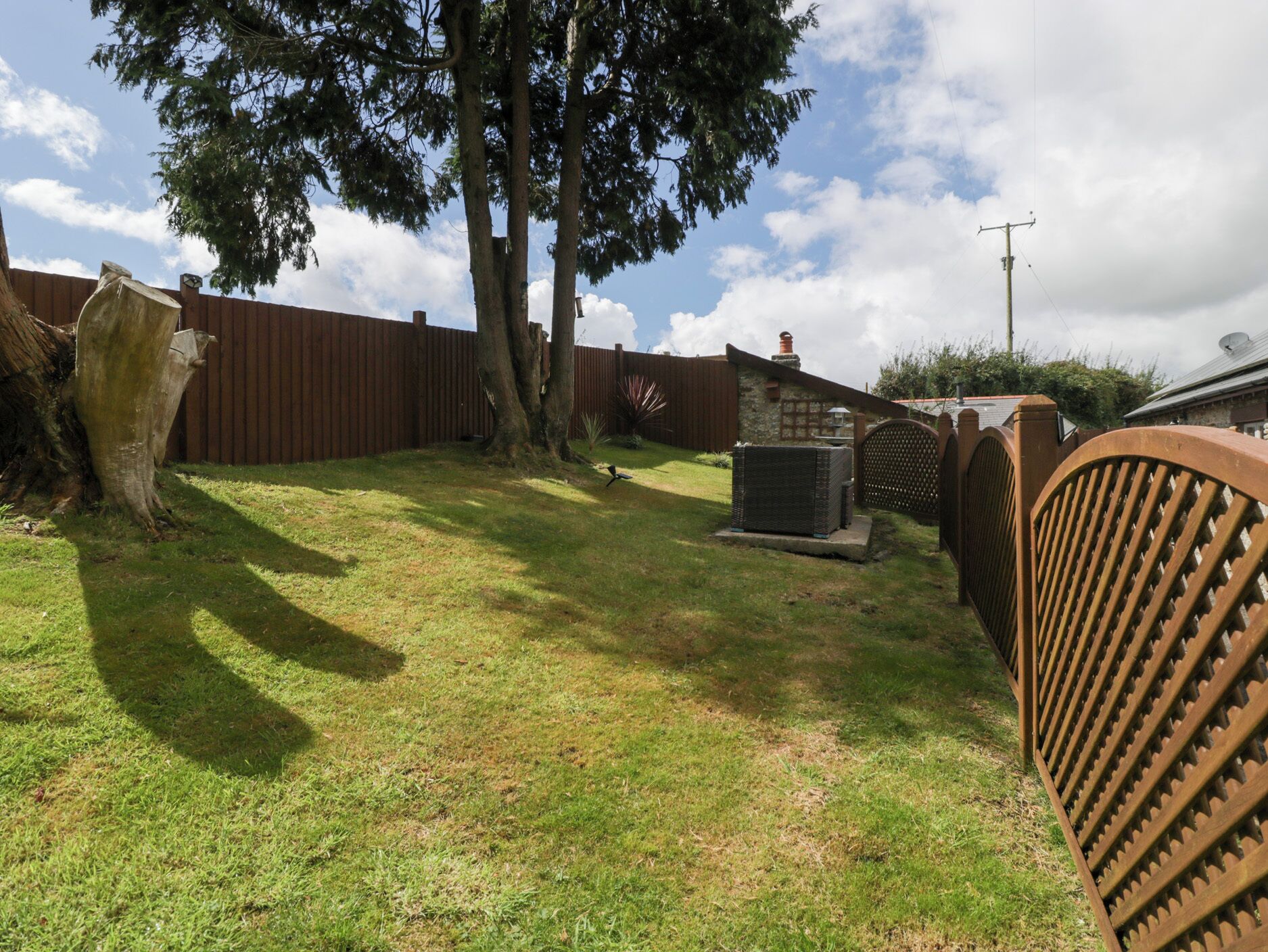 A backyard with a wooden fence, a large tree, and a small building.