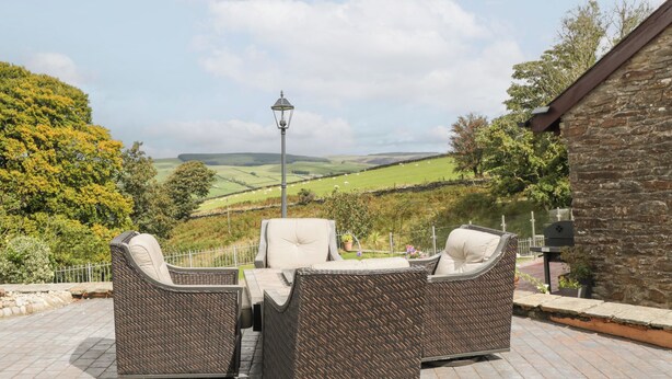 A patio with wicker furniture and a view of rolling hills. - Caner Bach Lodge (Bridgend)
