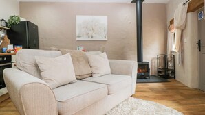 A living room with a beige sofa, a white shag rug, a fireplace, and a painting on the wall. - Caner Bach Lodge (Bridgend)