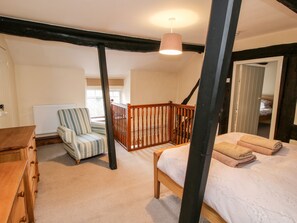 Une chambre à coucher comprenant un lit, une chaise, une commode en bois, un escalier et un luminaire suspendu.